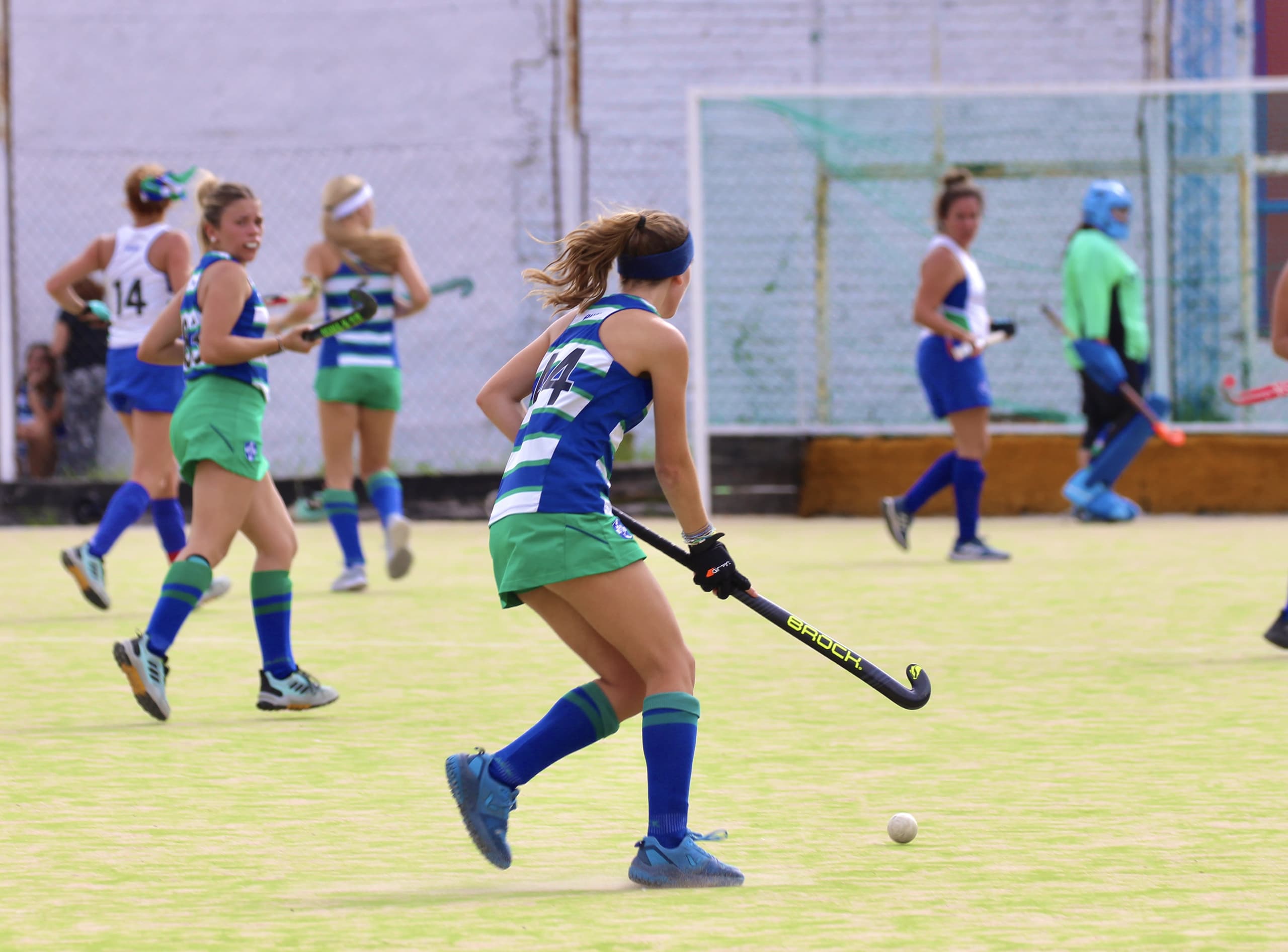 Una jugadora conduce la bocha hacia el arco durante un partido de hockey, con la arquera atenta al fondo.